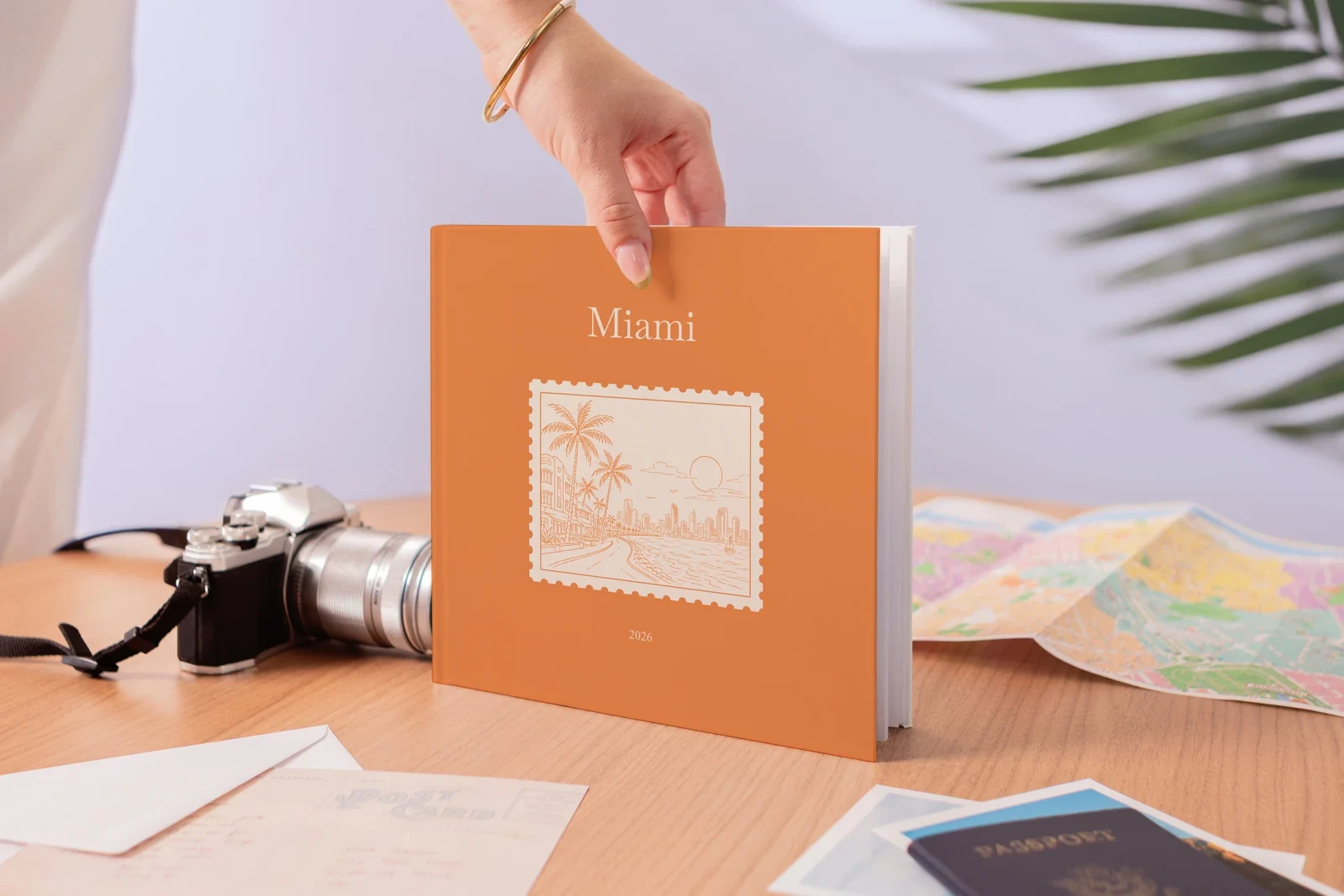 A hand holding a Miami hardcover Travel Book over a desk with a camera, map and passport