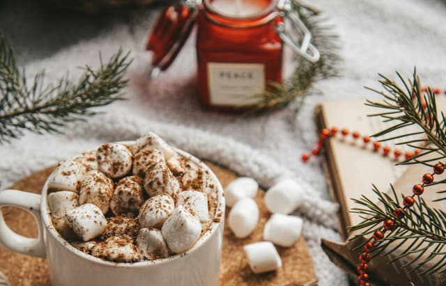 Mug of hot cocoa topped with marshmallows and a red candle in the background