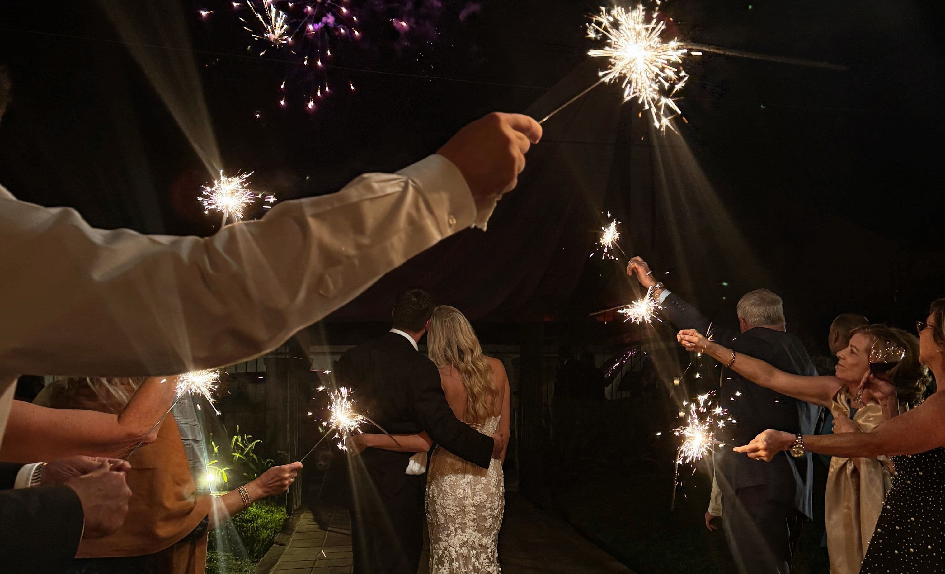 Wedding photo of the couple at night with guests holding sparklers