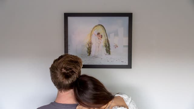 Couple with their back against the camera looking at a framed poster of their wedding