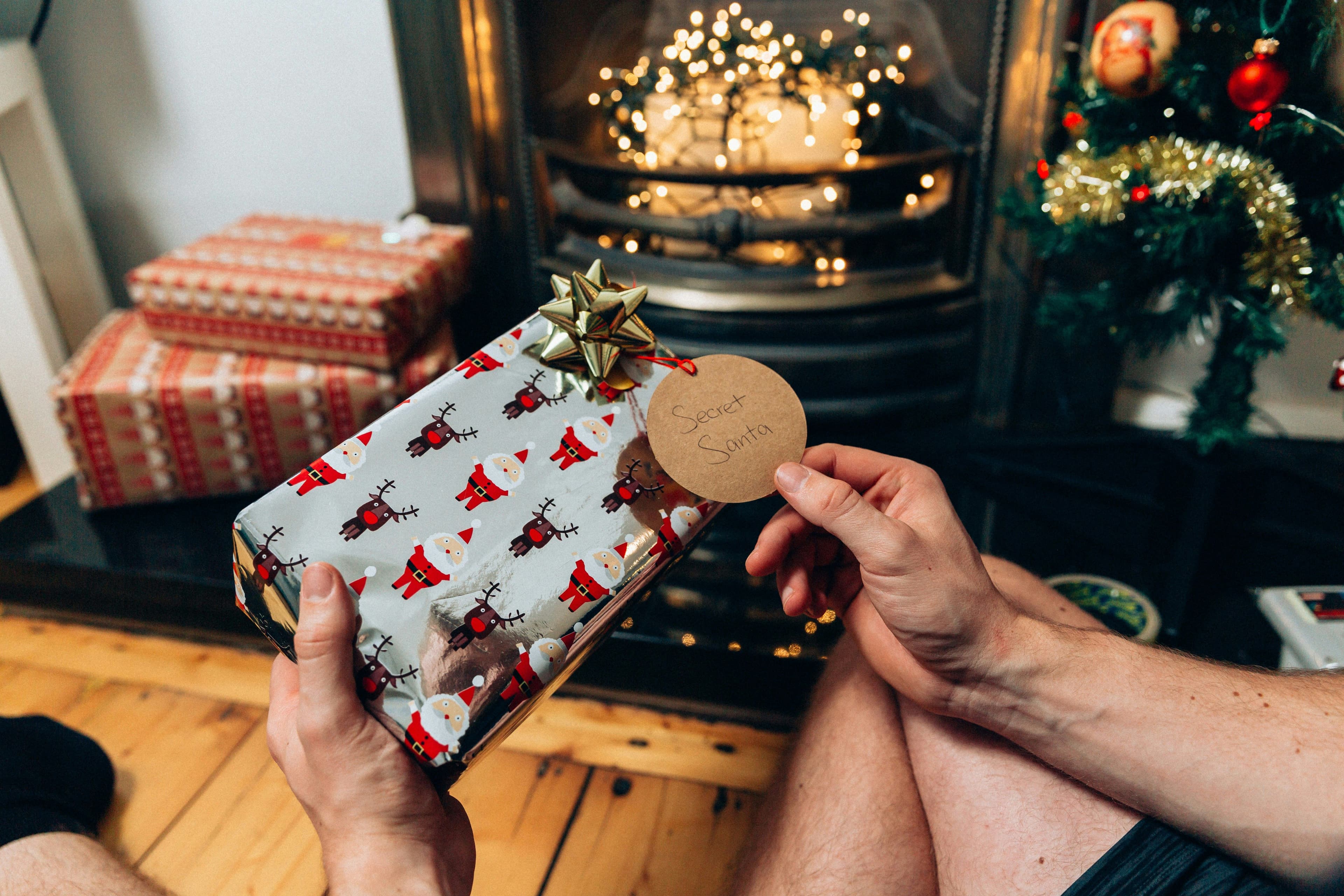 Present wrapped in pastel blue paper with patterns of Santa and reindeers in front of a fireplace with fairy lights in it